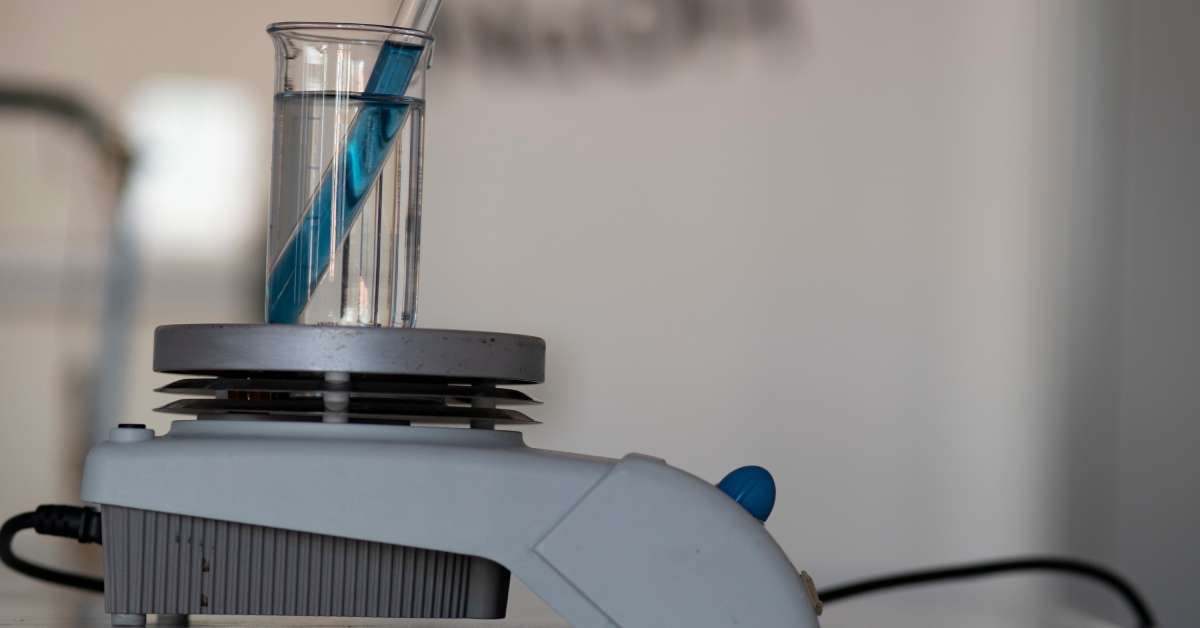 A glass beaker sitting on a hot plate magnetic stirrer. In the beaker are two glass test tubes full of a blue liquid.
