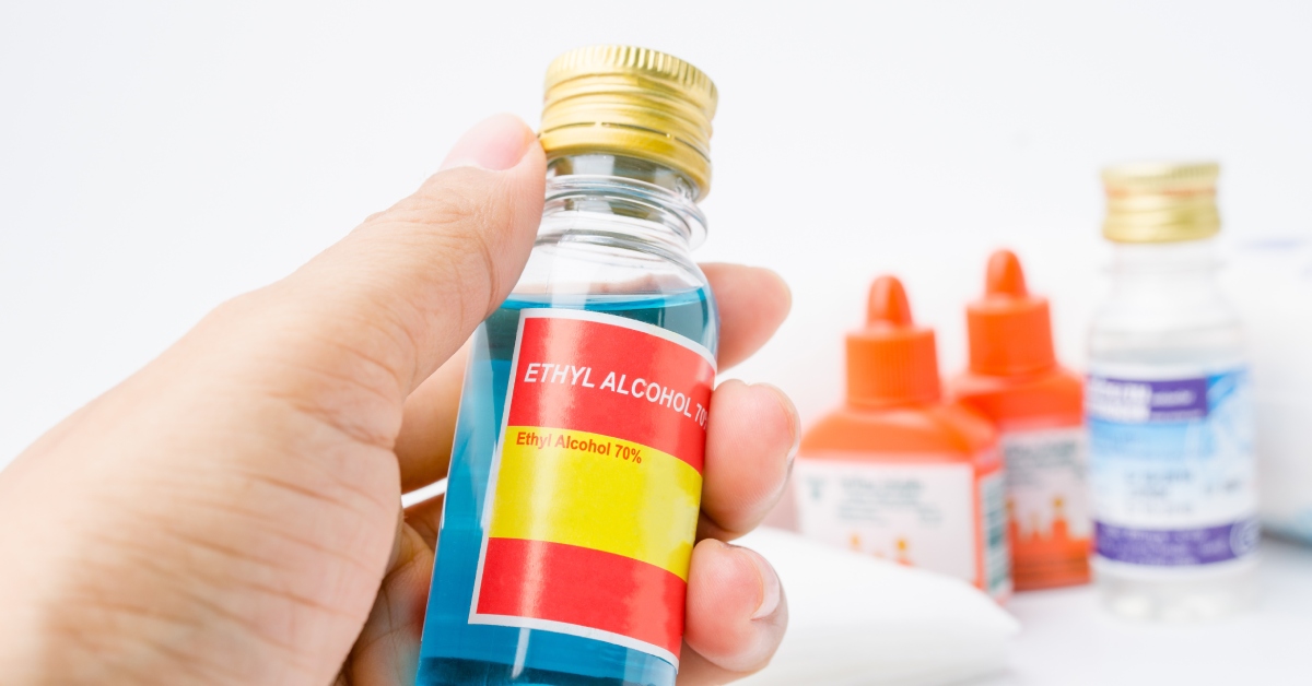 A person holding a bottle with blue liquid in it. The bottle has a label that says ethyl alcohol 70%.