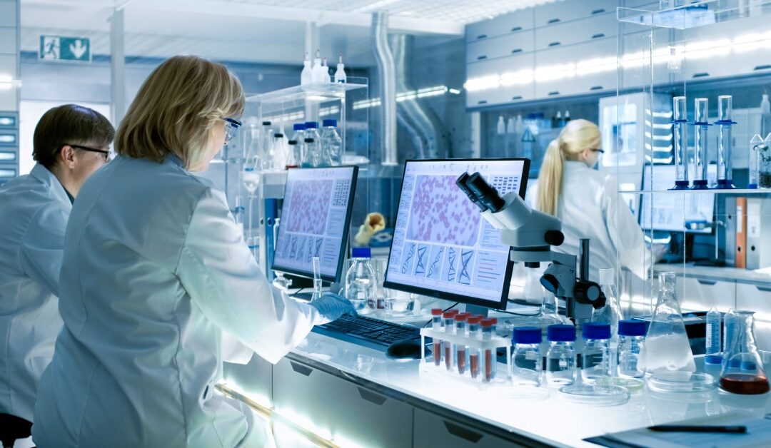 Three people are working a laboratory. There are two female scientists and one male scientist wearing eyeglasses and lab coats.