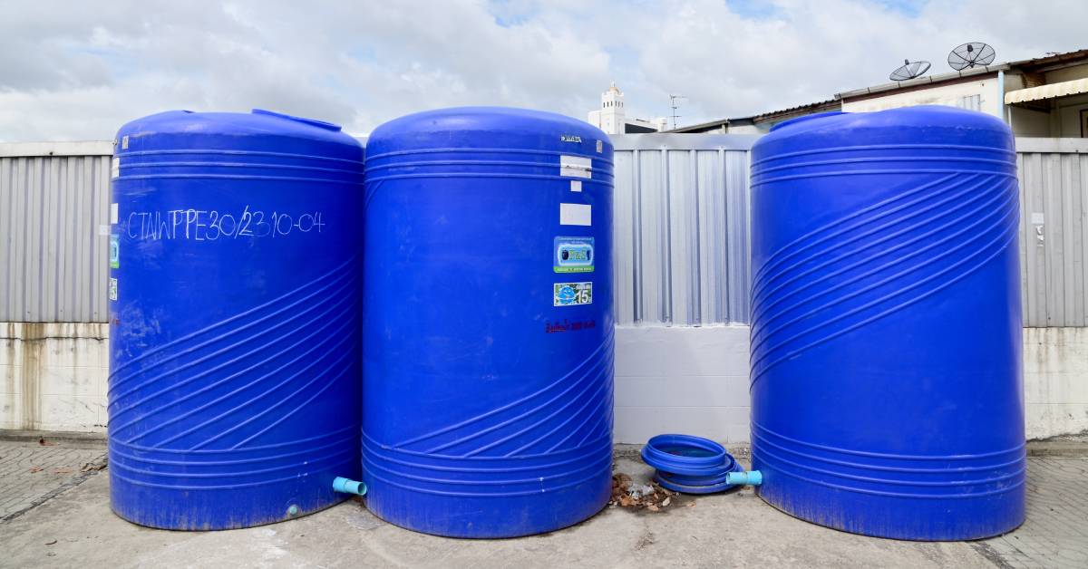 Three polyethylene drums placed next to each other along a low outdoor wall made of metal and concrete.