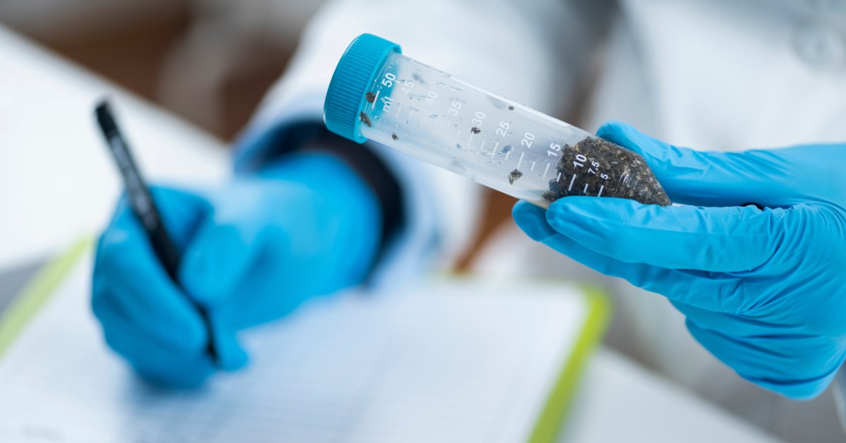 A lab worker holding a test tube filled with a substance. The lab worker is writing on a piece of paper.