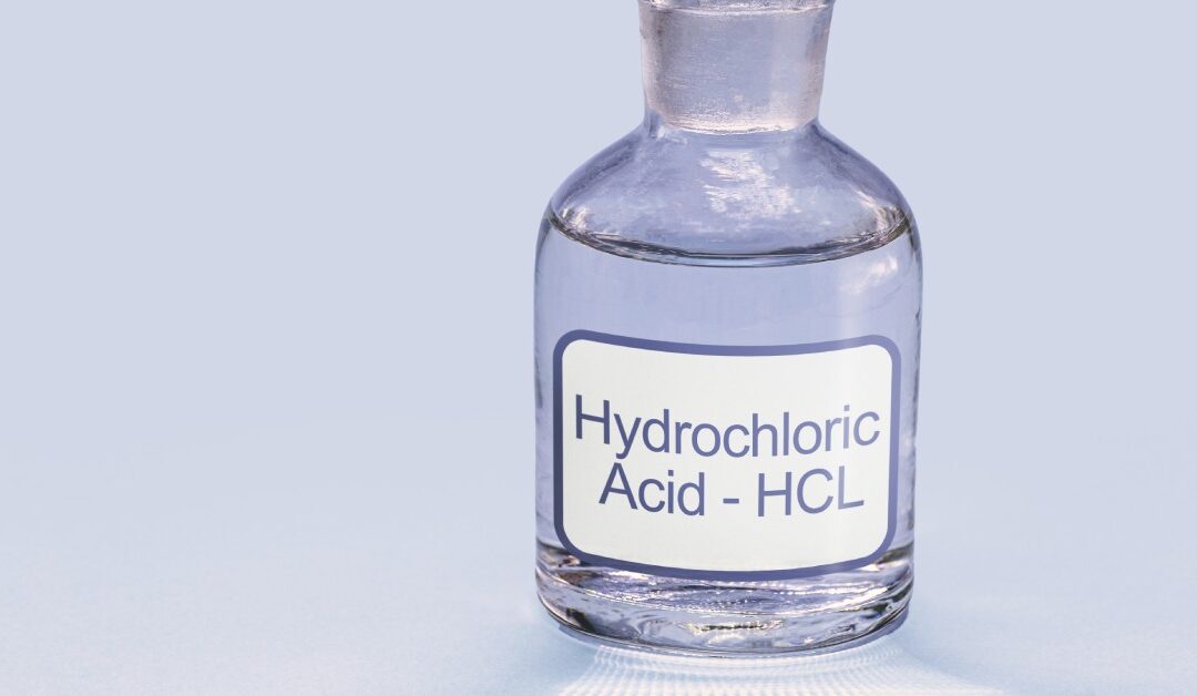 A clear bottle with a label that says Hydrochloric Acid - HCL. It's sitting in front of a white background.