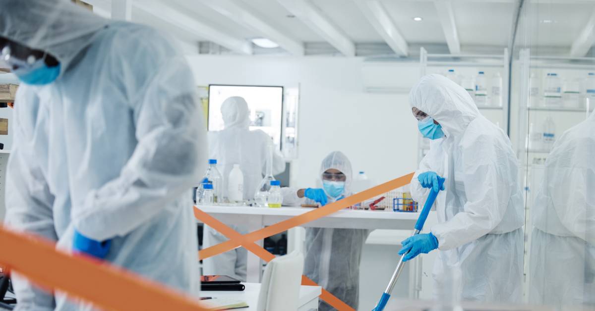 A group of people wearing protective suits, eyeglasses, and masks. Two people are cleaning the floors.